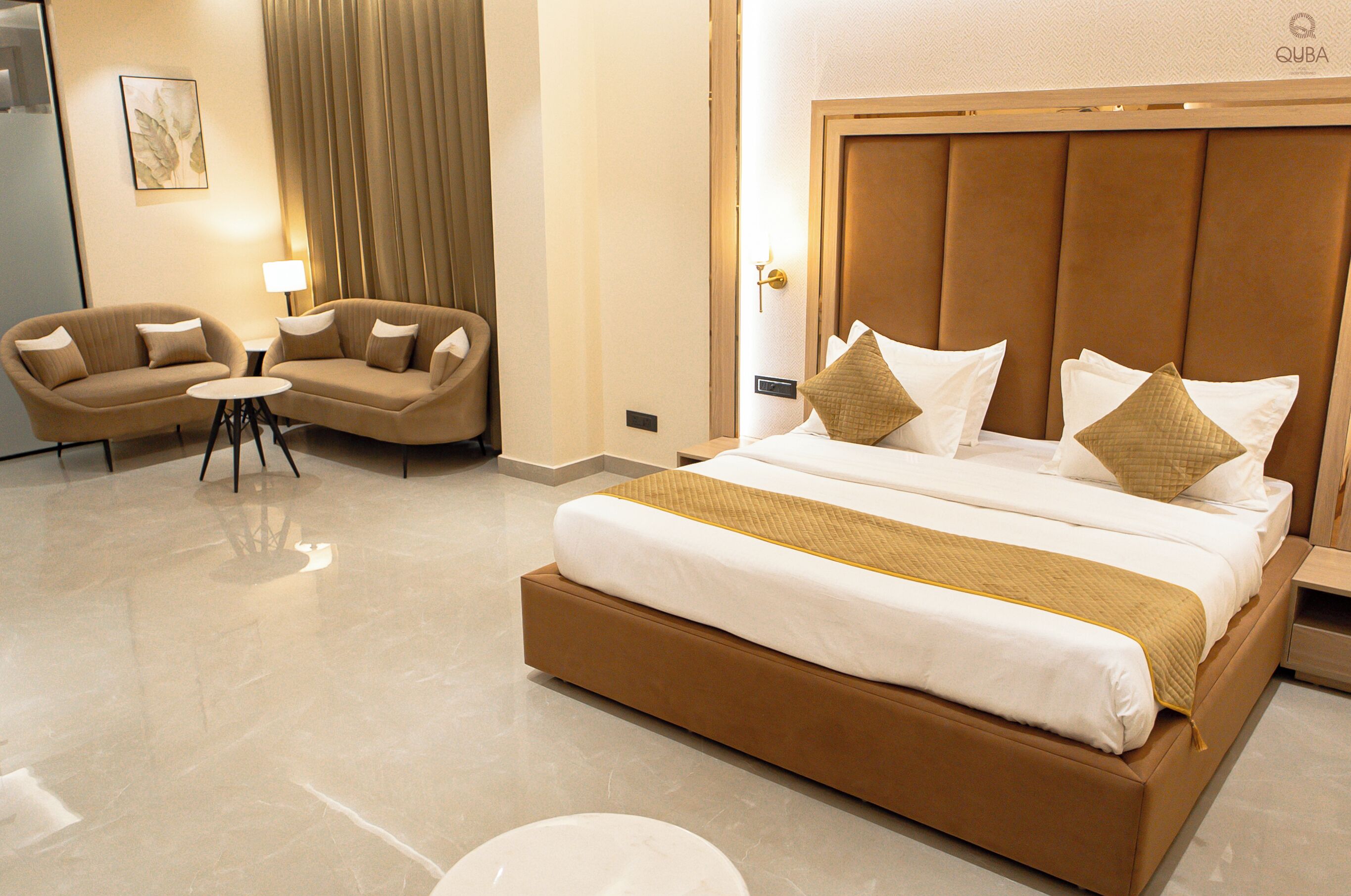 Une chambre d’hôtel avec un grand lit, deux fauteuils, une petite table et une lampe.