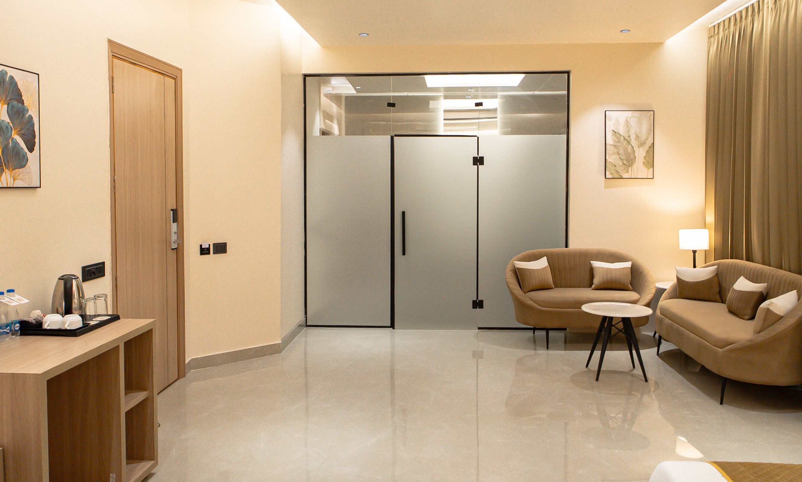 A hotel room with a sofa, a small table, a cabinet with toiletries, and a sliding door leading to a bathroom.