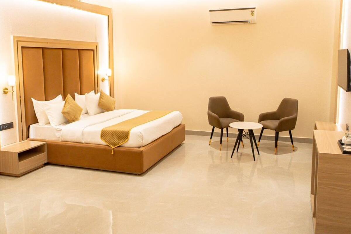 A modern hotel room with a large bed, bedside tables, a small round table, two armchairs, and a TV.