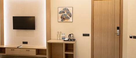 A hotel room with a flat-screen TV mounted on a textured wall, a wooden cabinet with a small table, a framed artwork, and a wooden door.