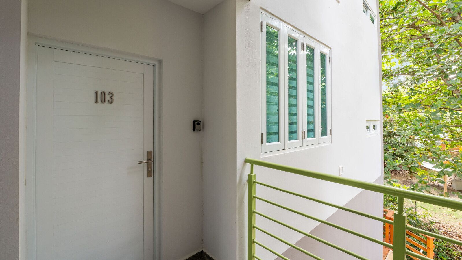 Eine weiße Tür mit der Nummer 103, ein geländer aus grünem Metall und ein Fenster mit satinierten Scheiben.