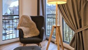 A modern room with a large window, a dark armchair with a fluffy throw, a floor lamp, and a view of a residential area.