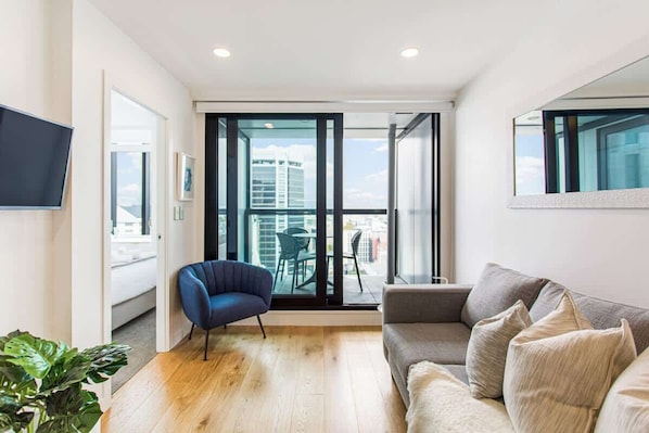 A modern living room with a sofa, a chair, and a TV. There is a balcony with a view of the city. - Modern 2BR in CBD w/ Full Amenities- Zodiak Stays (Auckland)