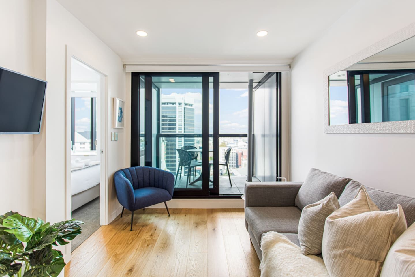 A modern living room with a sofa, a chair, a TV, and a balcony with a city view.