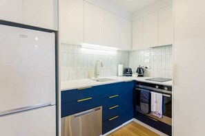 A modern kitchen with white cabinets, a blue countertop, and stainless steel appliances including a refrigerator, dishwasher, and oven. - Modern 2BR in CBD w/ Full Amenities- Zodiak Stays (Auckland)