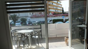 A balcony with a table and chairs, a view of parked cars, and a building with a sign in the background. - Apartment near beach for 2/4 ppl in Roses (Roses)