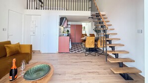 Una sala de estar moderna con un sofá, una zona de comedor con sillas, una escalera y una cocina al fondo.