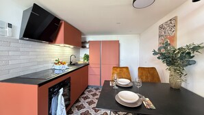 Cocina compacta con encimera negra, estufa y pileta. Hay una mesa de comedor con dos sillas y un florero con plantas.