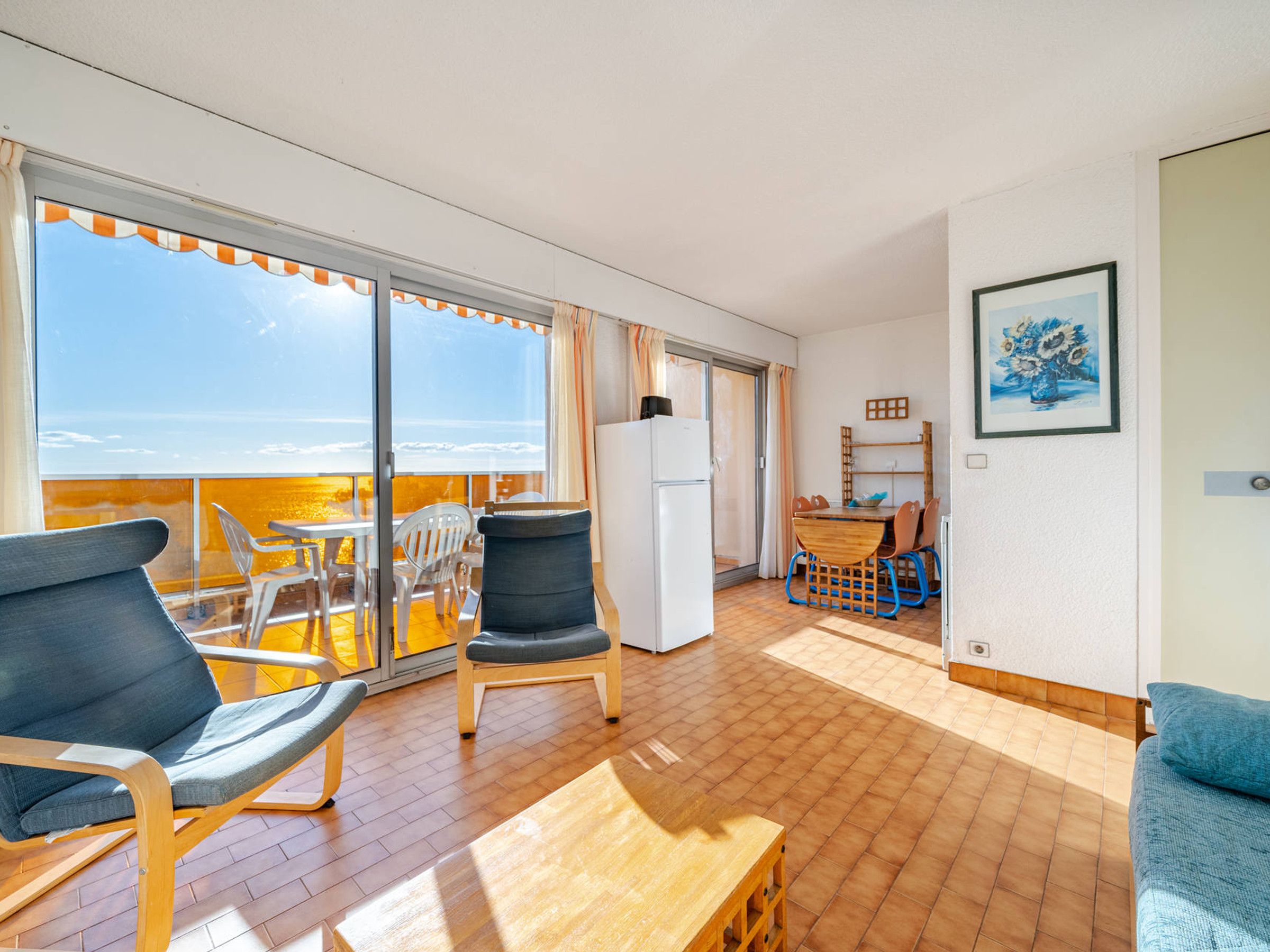 Un balcón con vista al mar, un comedor con mesa y sillas, y un refrigerador en la habitación.