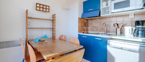 A compact kitchen with blue cabinets, a wooden dining table, and a microwave.
