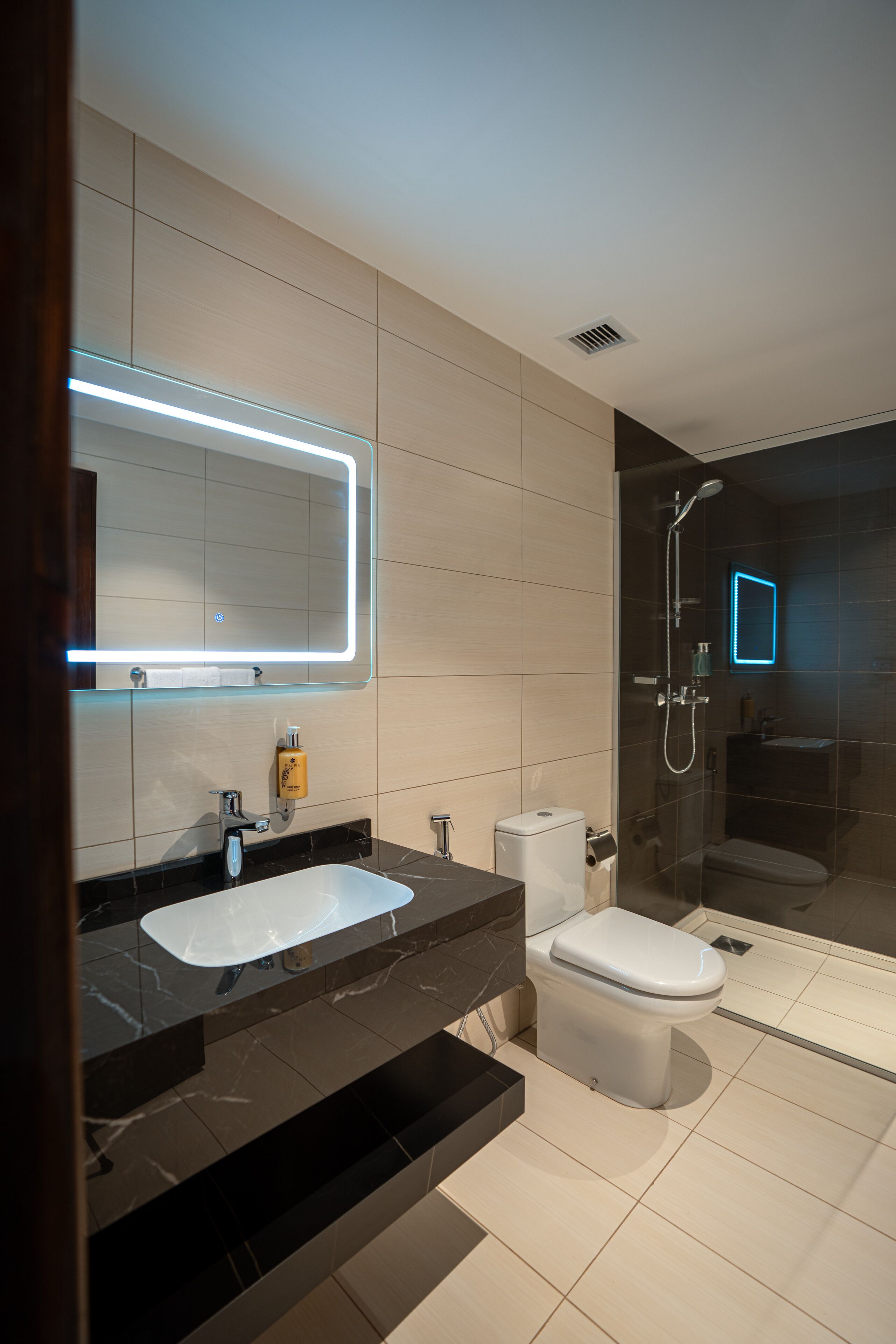 Une salle de bain moderne avec un grand miroir, un lavabo blanc, des toilettes et un espace douche.