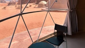 Tienda de campaña con vistas despejadas a un paisaje desértico, incluyendo formaciones rocosas y cielo claro.