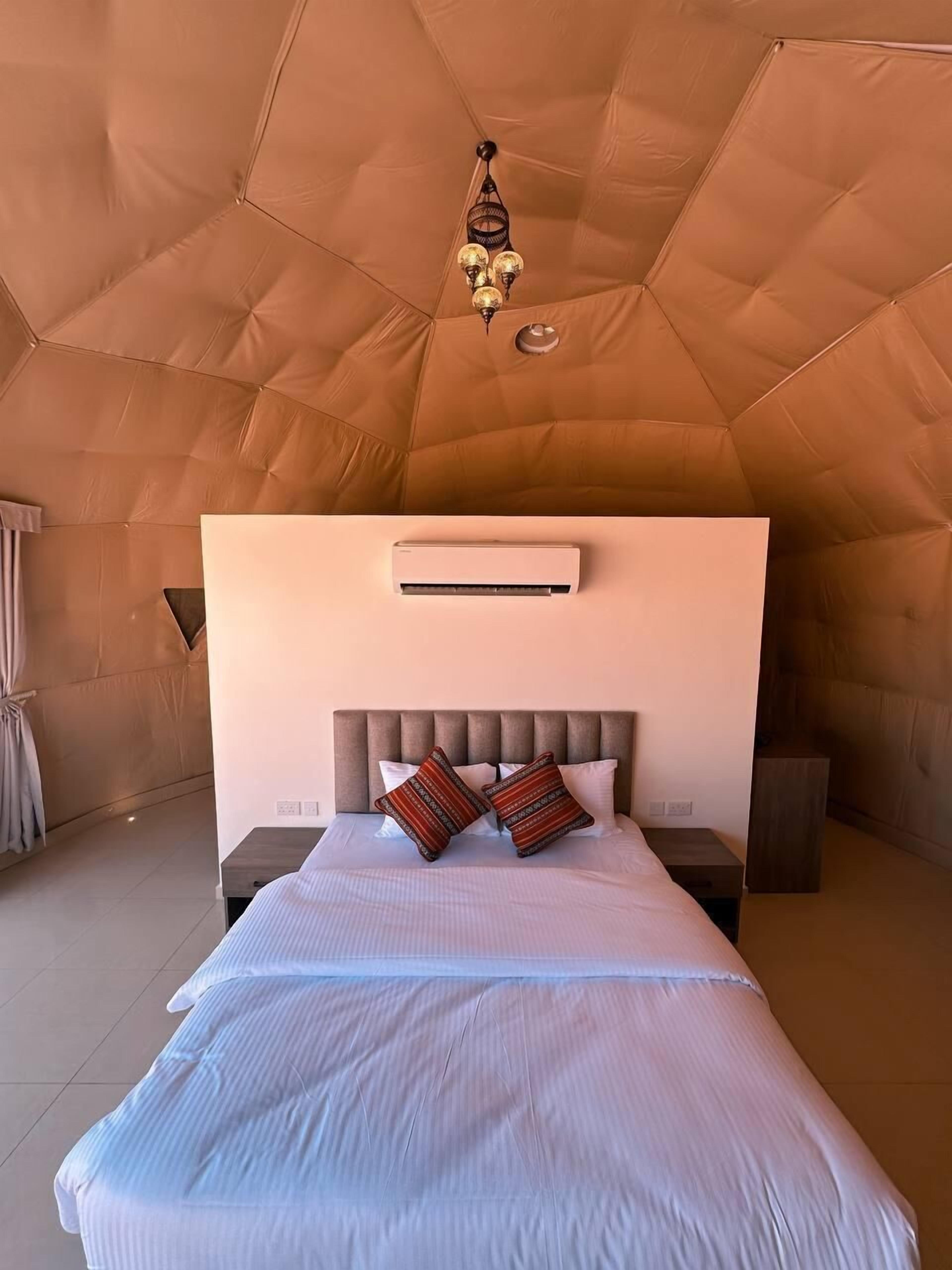 Ein geräumiger Zeltraum mit einem Bett, einer Hängeleuchte und einer Klimaanlage.