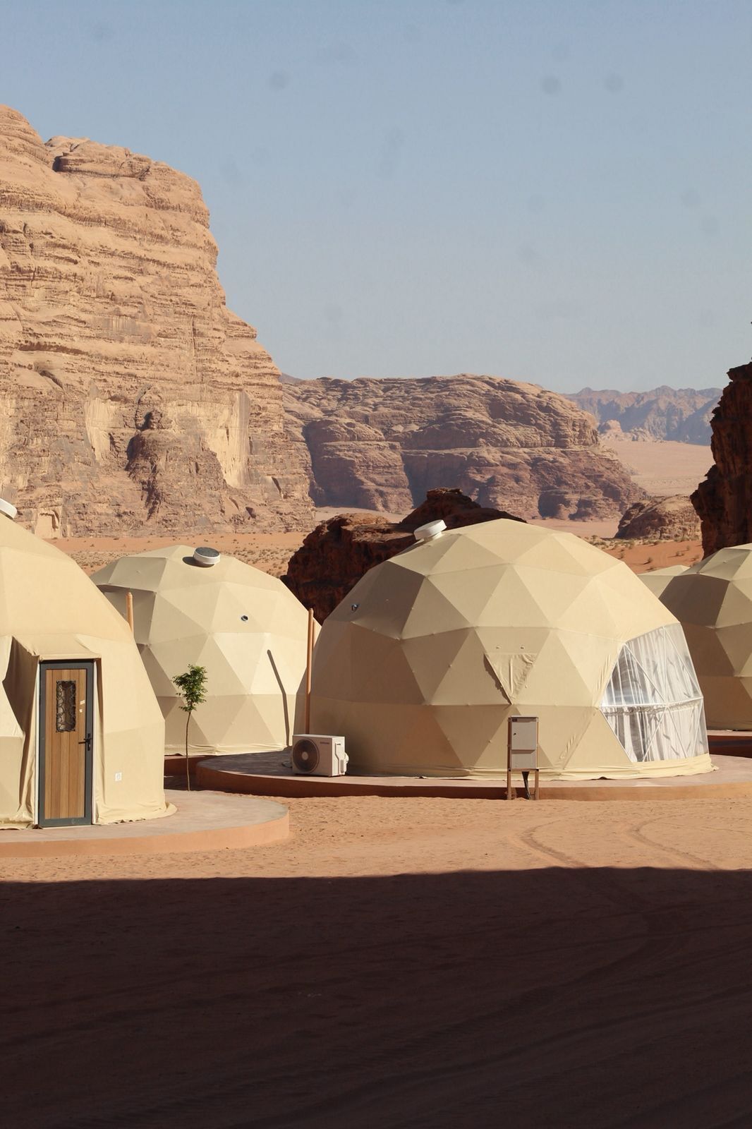 Des tentes en forme de dôme géodésique, installées dans un paysage désertique, avec des montagnes rocheuses en arrière-plan.
