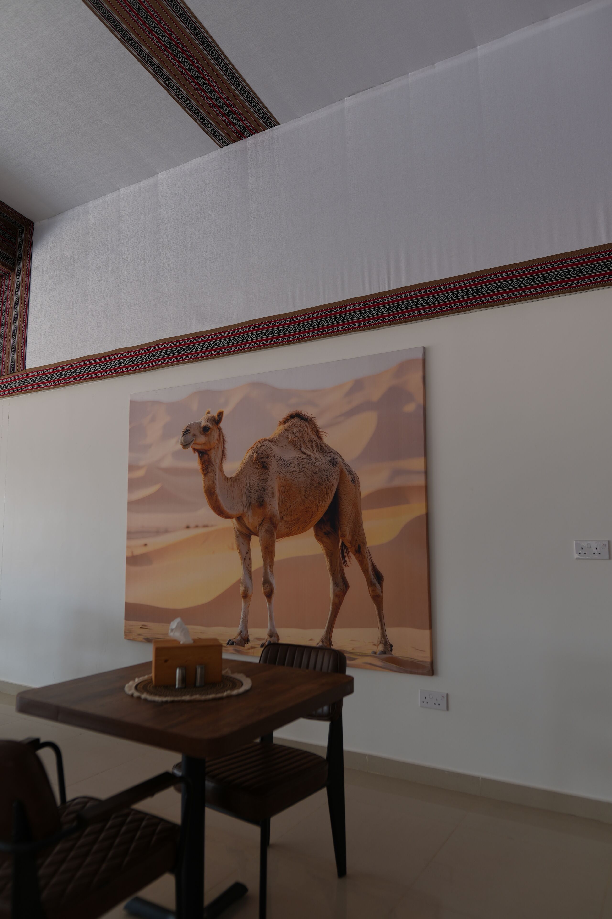 Un coin repas avec une table et des chaises, un tableau représentant un chameau accroché au mur, et une bordure décorative au-dessus du tableau.
