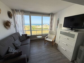 A living room with a sofa, armchair, TV, and a view of the beach. - T2 for 4 in Le Barcarès, beachfront, private parking (Le Barcarès)