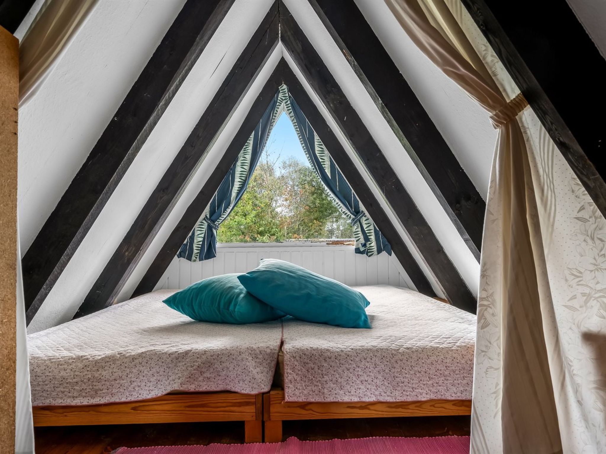 Ein kleines, dreieckiges Schlafzimmer im Dachgeschoss mit einem Bett, Kissen und einem Fenster.