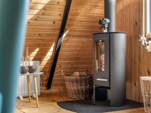 Un interior moderno con techo de paneles de madera, un estufa de leña negra, una cesta de mimbre y una pequeña mesa con objetos decorativos.