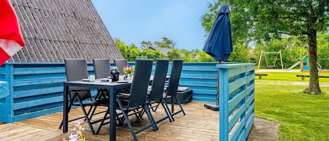 A wooden deck with a table and chairs, a blue fence, and a playground in the background.
