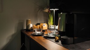 A dimly lit room with a wooden desk, a black coffee machine, a glass cup, and a vase with flowers. - MICELI EXCLUSIVE SUITE (Palermo)