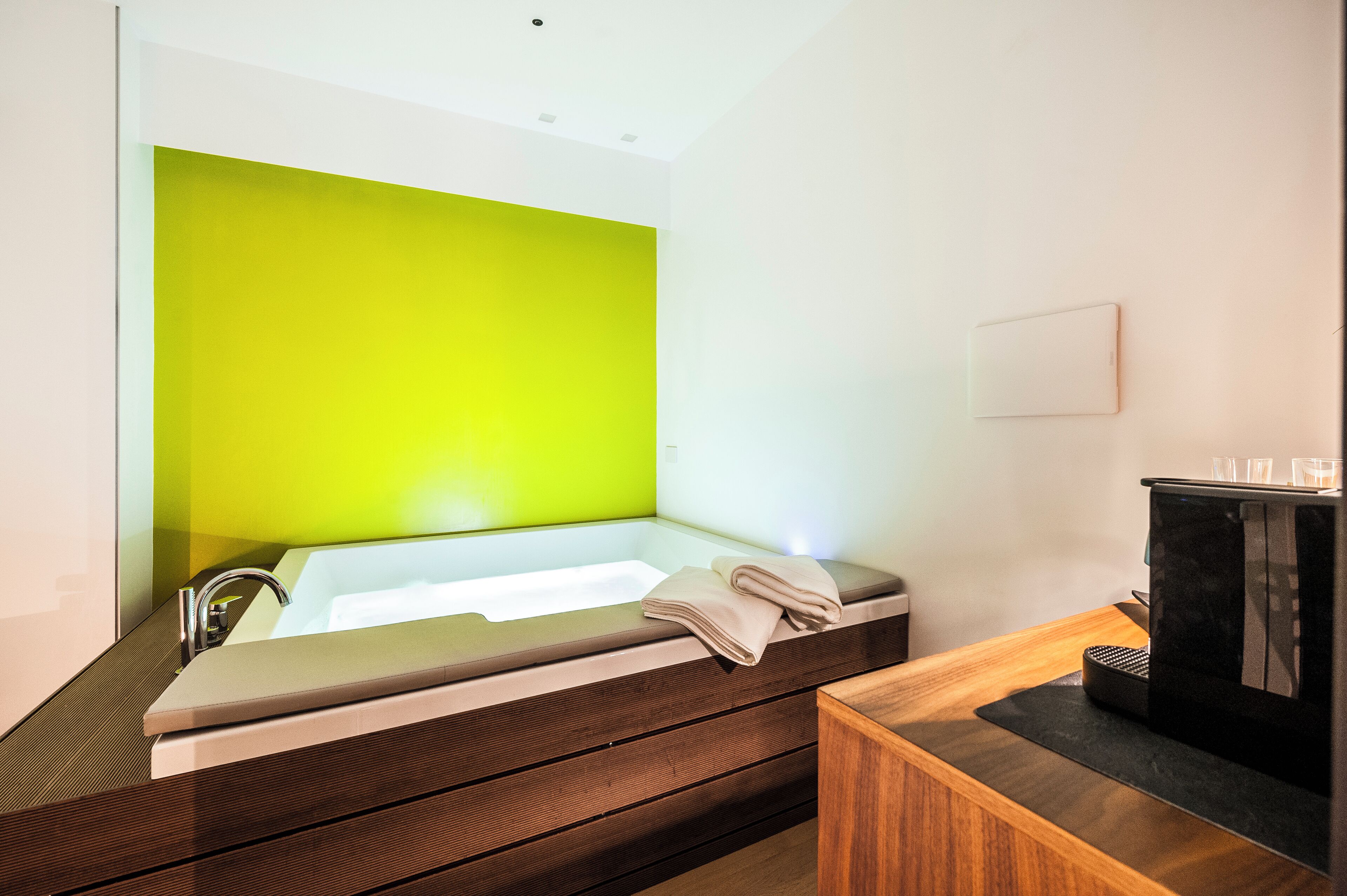 A modern bathroom with a large bathtub, a wooden vanity, and a coffee machine.