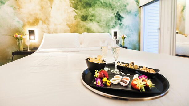 A hotel room with a bed, a tray with snacks and drinks, and a wall with a textured mural. - MICELI EXCLUSIVE SUITE (Palermo)
