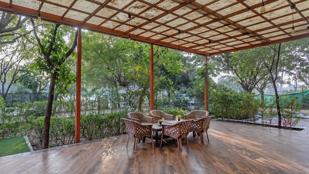 An outdoor covered patio with a wooden table and chairs, surrounded by greenery and trees. - Treebo Executive Suites (Gandhinagar)