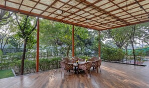 An outdoor covered patio with a wooden table and chairs, surrounded by greenery and trees. - Treebo Executive Suites (Gandhinagar)