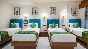 A hotel room with four beds, each with a blue headboard and colorful patterned bedspreads. There are wall-mounted light fixtures and framed artwork above each bed. - Treebo Executive Suites (Gandhinagar)
