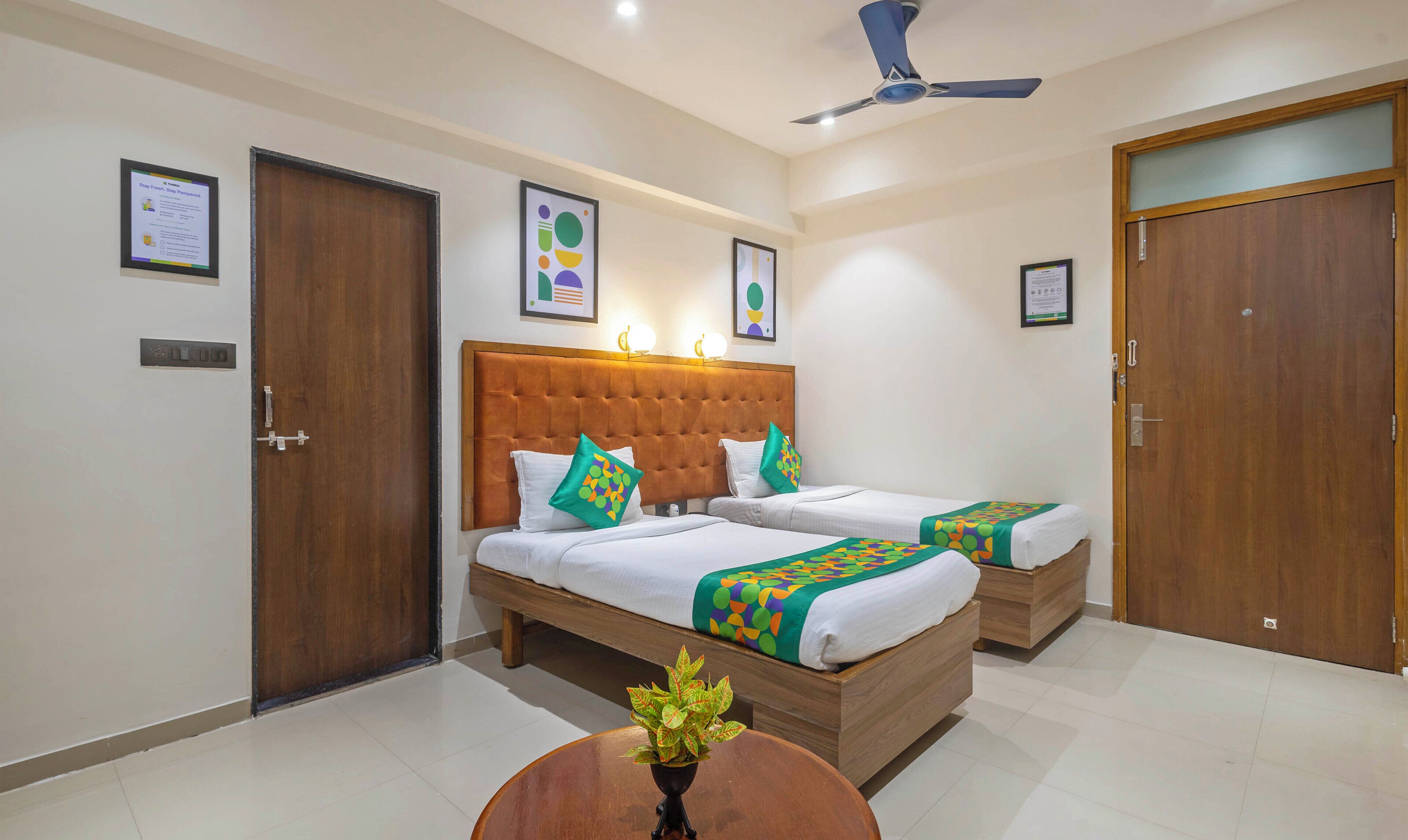 A hotel room with two beds, a wooden headboard, a ceiling fan, and a small table with a plant.