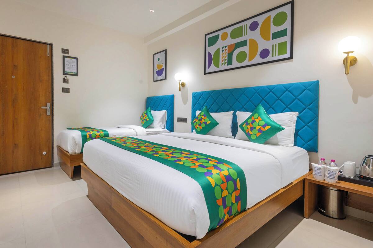 A hotel room with two beds, a wooden floor, a blue headboard, and a framed abstract painting on the wall.
