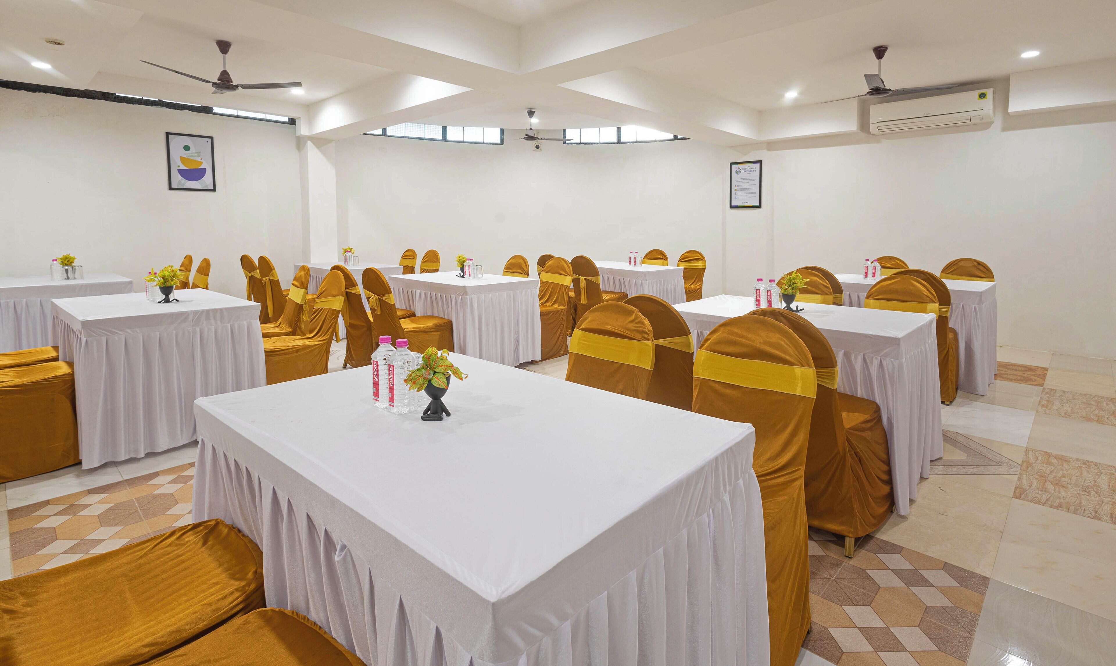 A conference room with multiple tables and chairs, white tablecloths, and golden chair covers.