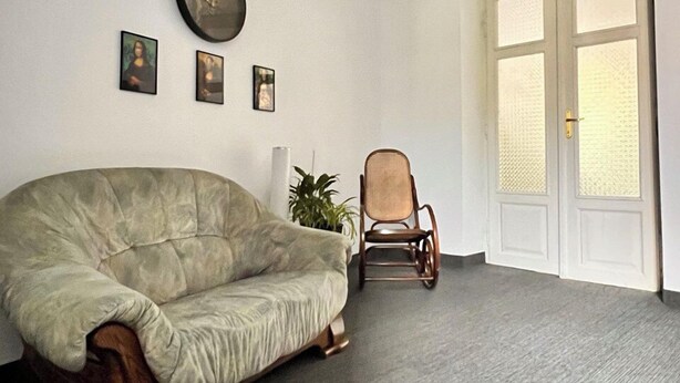 A spacious room with a large, plush sofa, a wooden rocking chair, and a wall clock. - Hostel Uno (Kraków)