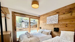 A hotel room with two beds, a wooden headboard, a large window with a view of buildings, and a wall-mounted artwork.