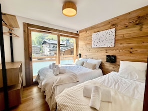 Une chambre d’hôtel avec deux lits, une tête de lit en bois, une grande fenêtre donnant sur des immeubles et une œuvre d’art accrochée au mur.