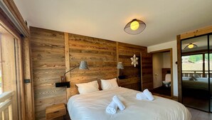A bedroom with a wooden wall panel, a bed with white linens, two bedside lamps, and a ceiling light fixture.