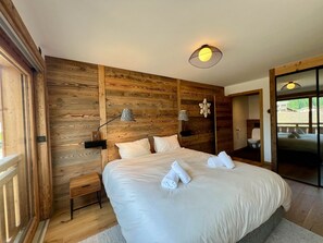 Une chambre avec un lambris en bois, un lit recouvert de draps blancs, deux lampes de chevet et un luminaire au plafond.