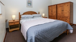Una camera da letto con un grande letto, comodini in legno, un armadio in legno e un quadro appeso al muro.