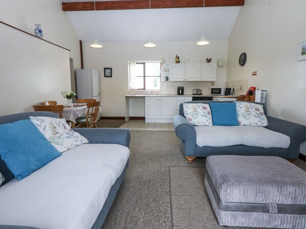 A compact living space with two sofas, a dining table, and a kitchenette. - Florence Cottage (Holyhead)