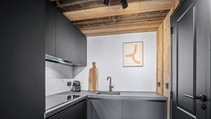 A modern kitchen with dark cabinetry, a wooden ceiling, and a minimalist design. - Renovated duplex in central Val Thorens with wifi (Val Thorens)