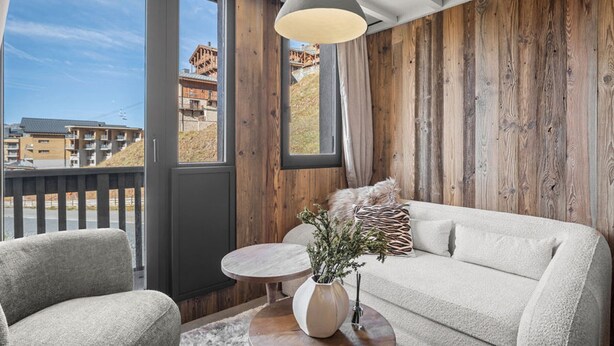 A room with a wooden wall, a sofa, a chair, a small round table, and a hanging light fixture. - Renovated duplex in central Val Thorens with wifi (Val Thorens)