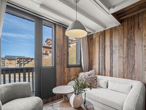 Une pièce avec un mur en bois, un canapé, une chaise, une petite table ronde et un luminaire suspendu.