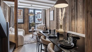 A modern dining area with a wooden interior, a large window with a view of a snowy landscape, and a cozy seating arrangement. - Renovated duplex in central Val Thorens with wifi (Val Thorens)