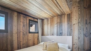 A bedroom with wooden walls, a large bed with white linens, and a fur throw. - Renovated duplex in central Val Thorens with wifi (Val Thorens)
