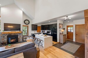 A spacious living area with a fireplace, a large island with bar stools, and a kitchen with dark cabinets and a refrigerator.