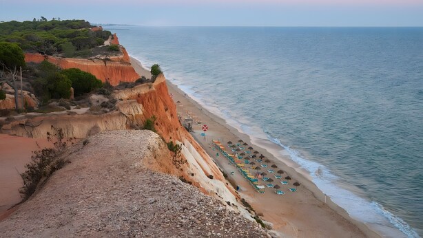 Un paisaje costero con playa, acantilados y una hilera de sombrillas de playa.