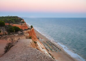 Un paisaje costero con playa, acantilados y una hilera de sombrillas de playa.