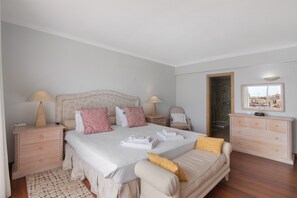 Un dormitorio con cama, mesitas de noche, cómoda y vistas a través de una ventana.