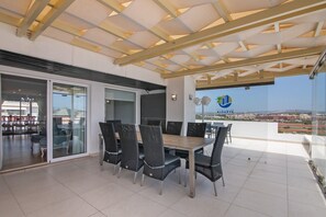 Un área de comedor al aire libre con techo, una mesa y sillas, un vidrio que da a un espacio interior y un logotipo en la pared.