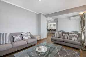 Una sala moderna con dos sofás grises, cojines a rayas, una mesa de centro de vidrio y una lámpara de pie contemporánea.